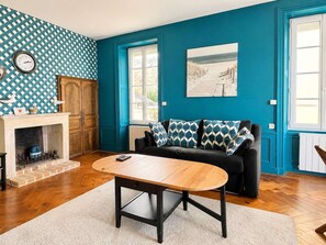 A living room with a blue wall, a fireplace, a sofa with patterned cushions, and a wooden coffee table.