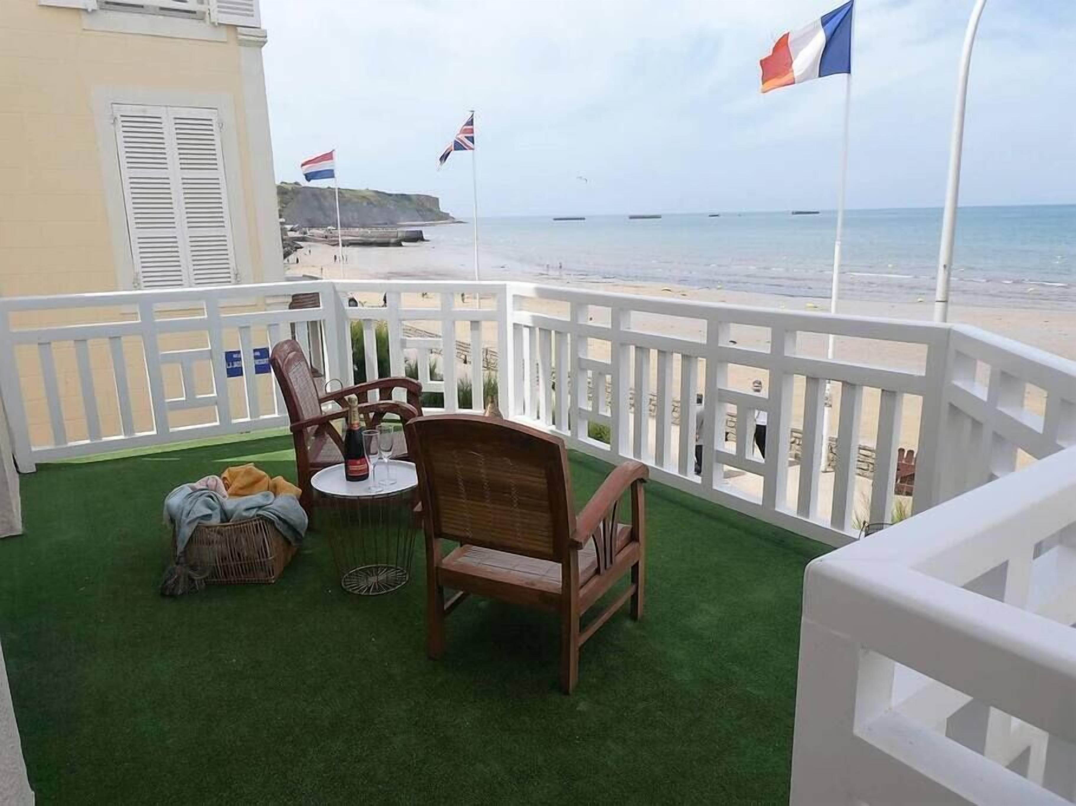Un balcon avec vue sur la plage, comprenant une table avec des chaises, une bouteille de champagne et un panier.