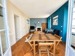 A dining area with a wooden table and chairs, a fireplace, and a blue accent wall. - Evasion vue mer D-Day pontoons, quai Arromanches (Arromanches-les-Bains)