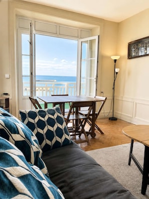 Una habitación con vistas al mar, una mesa de comedor con sillas, un sofá con cojines estampados y una lámpara de pie.