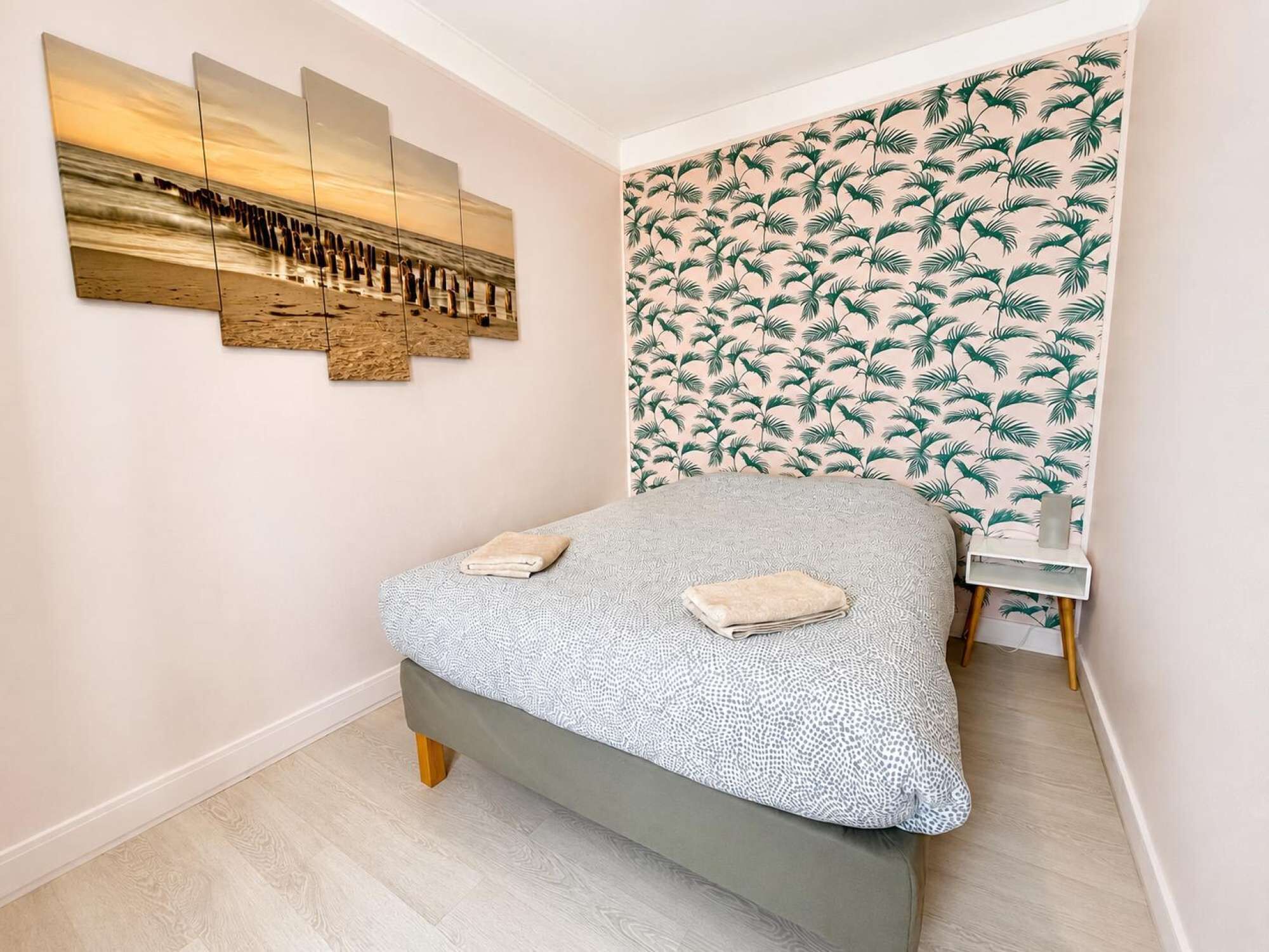Une chambre à coucher avec un lit, une œuvre d’art accrochée au mur, un papier peint à motifs et une petite table de chevet.