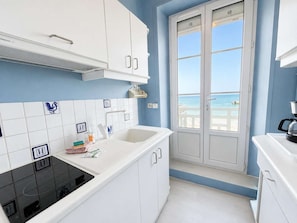Una cocina moderna con armarios blancos, una estufa negra y vista al mar a través de una puerta.