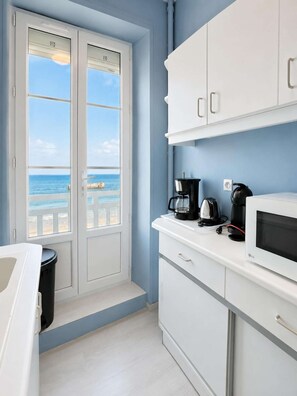 A kitchenette with a view of the ocean, white cabinets, a microwave, and a coffee maker. - Evasion vue mer D-Day pontoons, quai Arromanches (Arromanches-les-Bains)