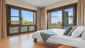 Um quarto espaçoso com uma cama grande, piso de madeira e amplas janelas com vista para o exterior.