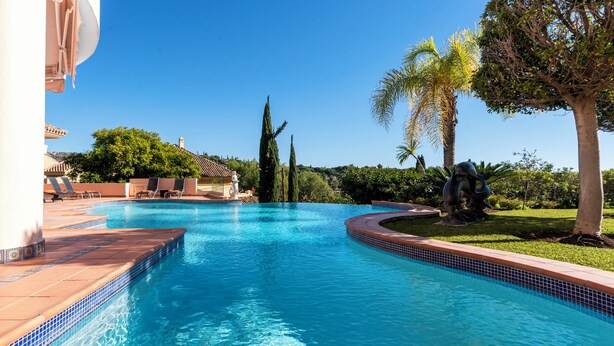 Piscina com borda azulejada, rodeada por espreguiçadeiras e uma estátua.