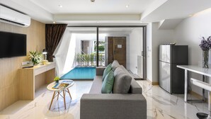 A modern living room with a grey sofa, a small round table, and a flat-screen TV mounted on the wall. - The Beachfront Hotel Phuket (Rawai)