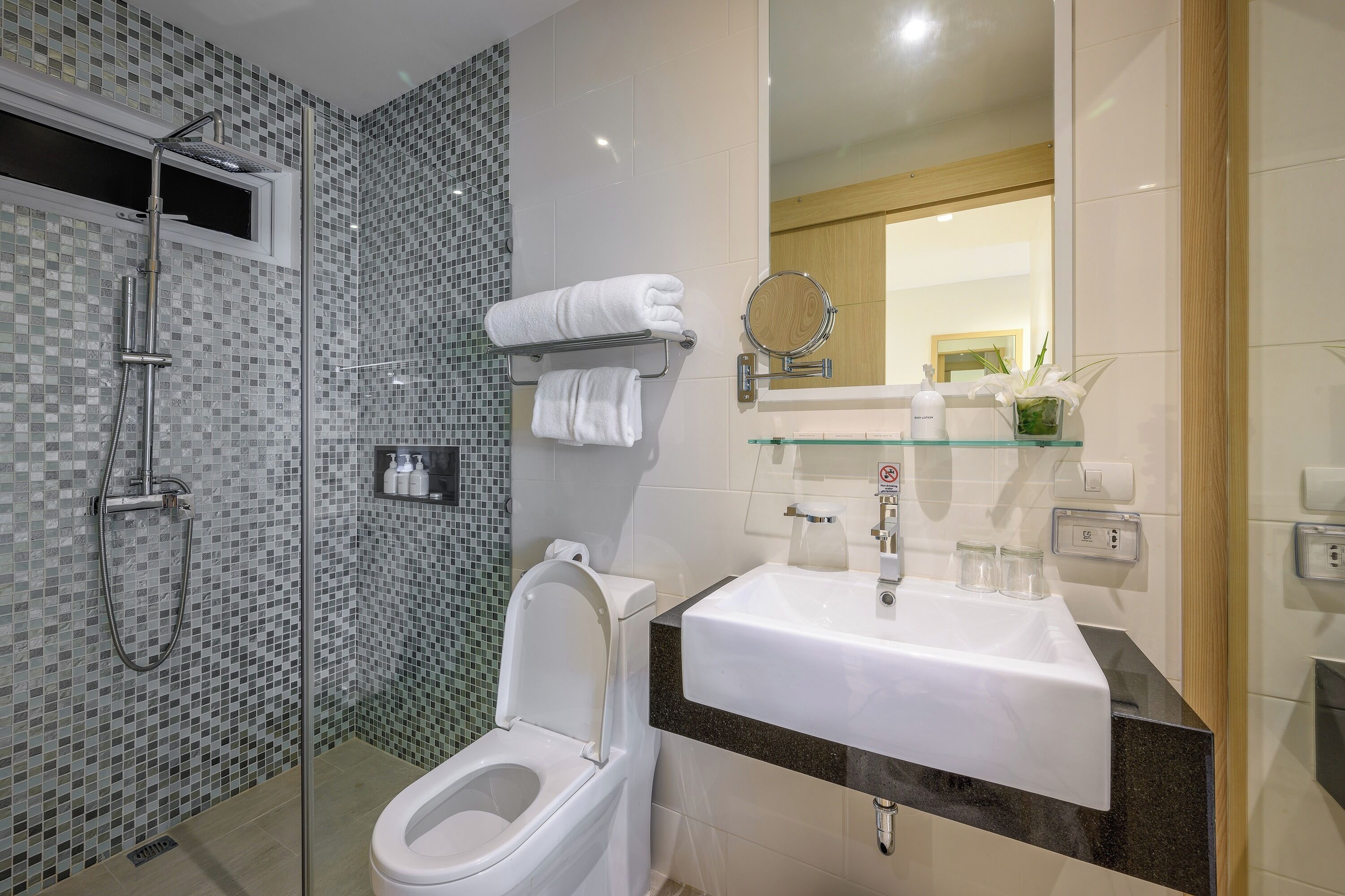 Een moderne badkamer met een glazen douchecabine, een wit toilet, een wastafel met een spiegel erboven en een klein raam.