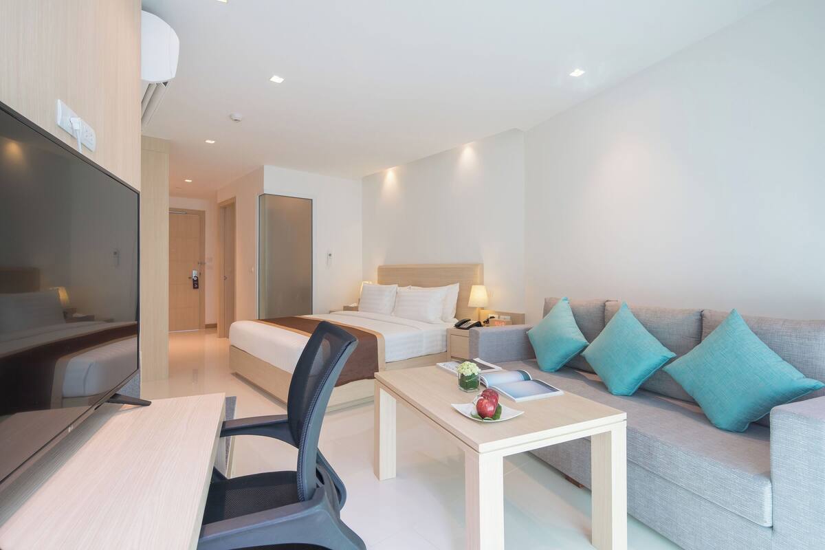 A modern hotel room with a bed, a sofa, a desk, and a TV.