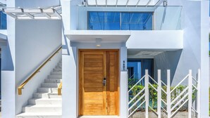 A modern two-story building with a wooden door, white exterior walls, and a glass balcony. - The Beachfront Hotel Phuket (Rawai)