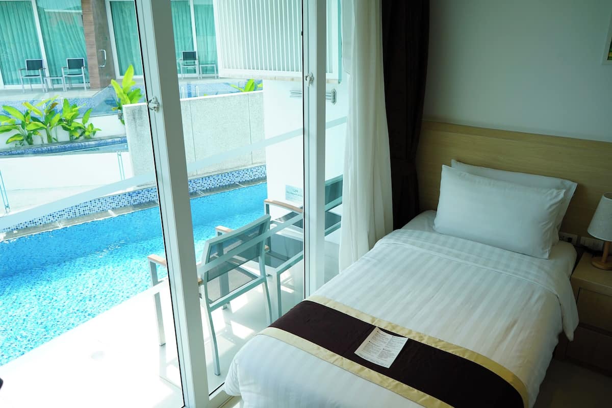 A hotel room with a bed, a nightstand, and a view of a swimming pool and outdoor seating area.