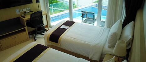 A hotel room with two beds, a desk with a computer, a TV, and a view of a pool and outdoor area.
