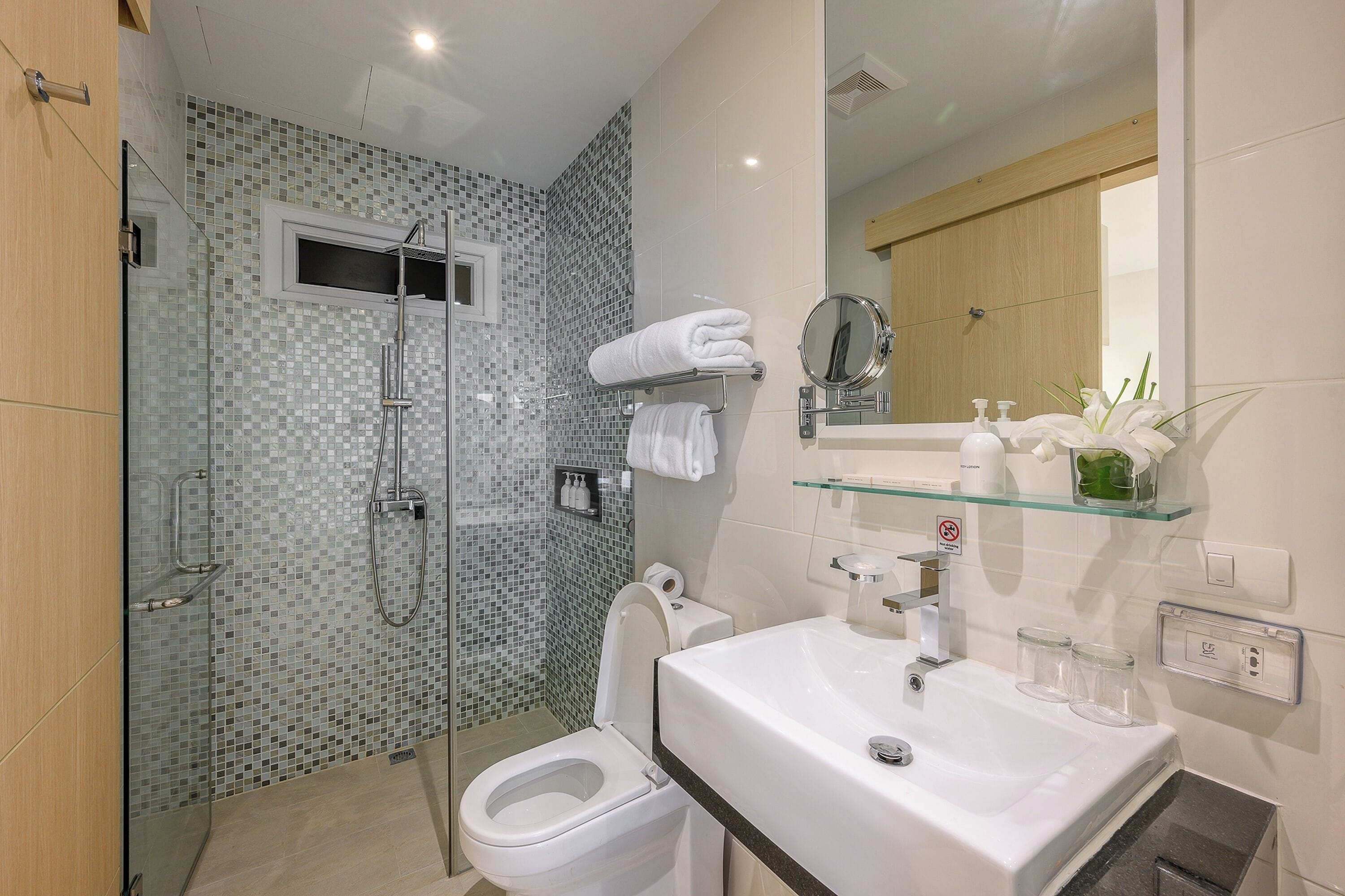 Un baño moderno con ducha de vidrio, inodoro blanco y lavamanos con espejo.