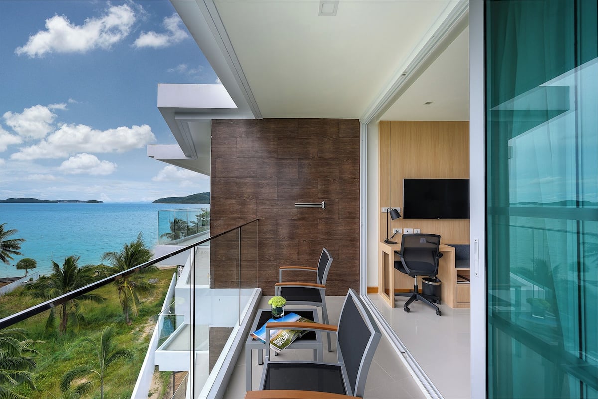 A balcony with a view of the sea, a desk with a chair, and a TV in a room.