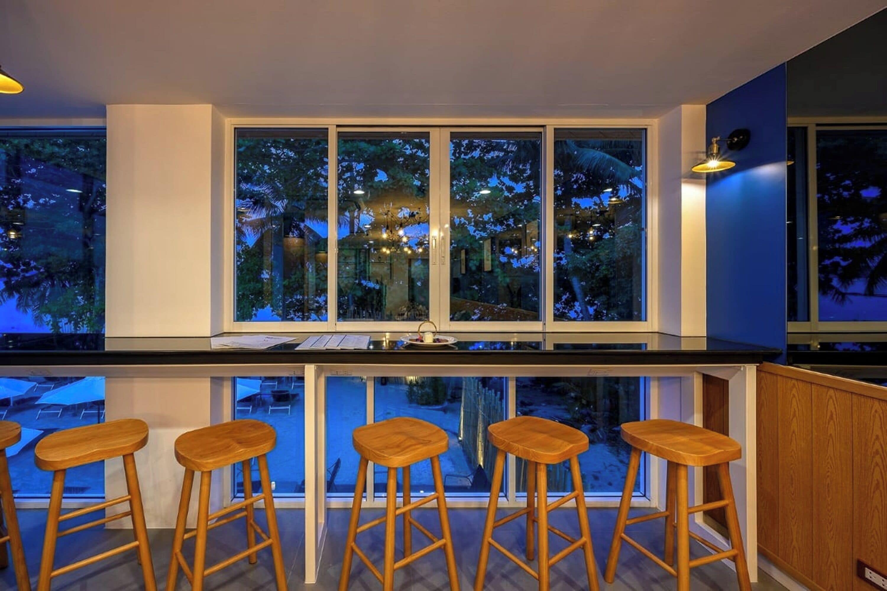 A kitchen with a large window, wooden stools, and a bar area.