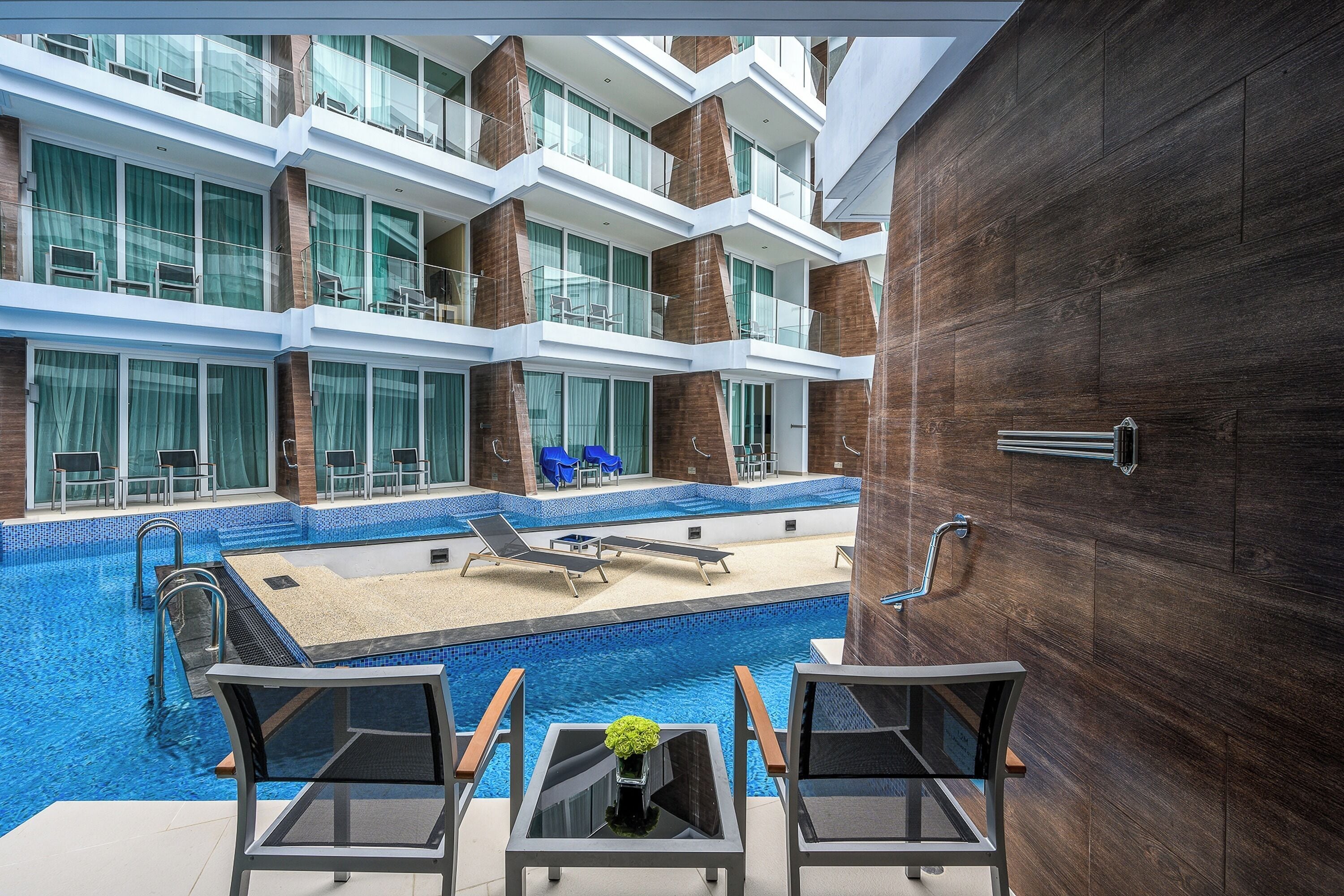 Un hotel moderno con una piscina infinita en la azotea, varios balcones y vistas al horizonte de la ciudad.