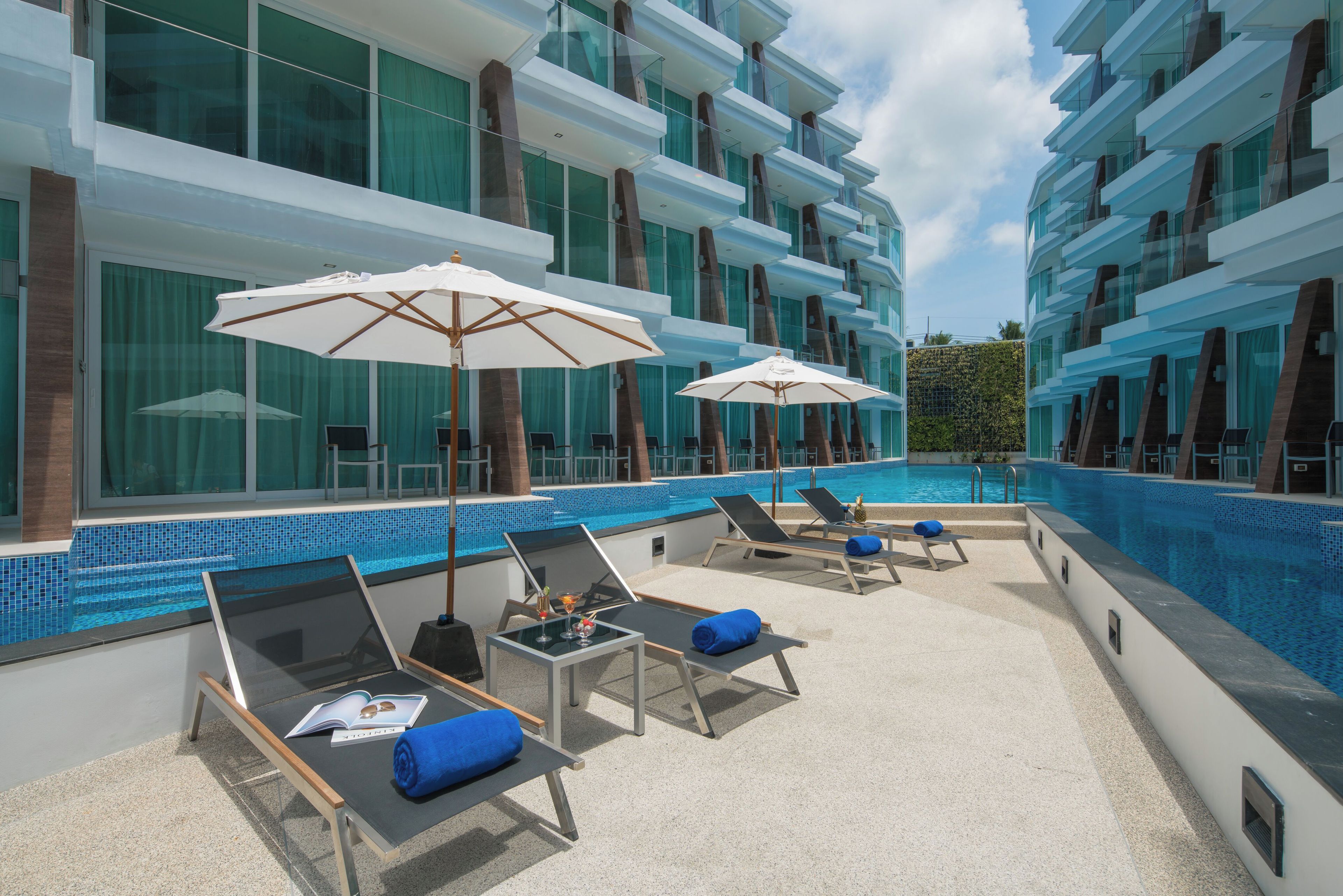 A poolside area with lounge chairs and umbrellas, a tiled pool, and a modern building with large windows.