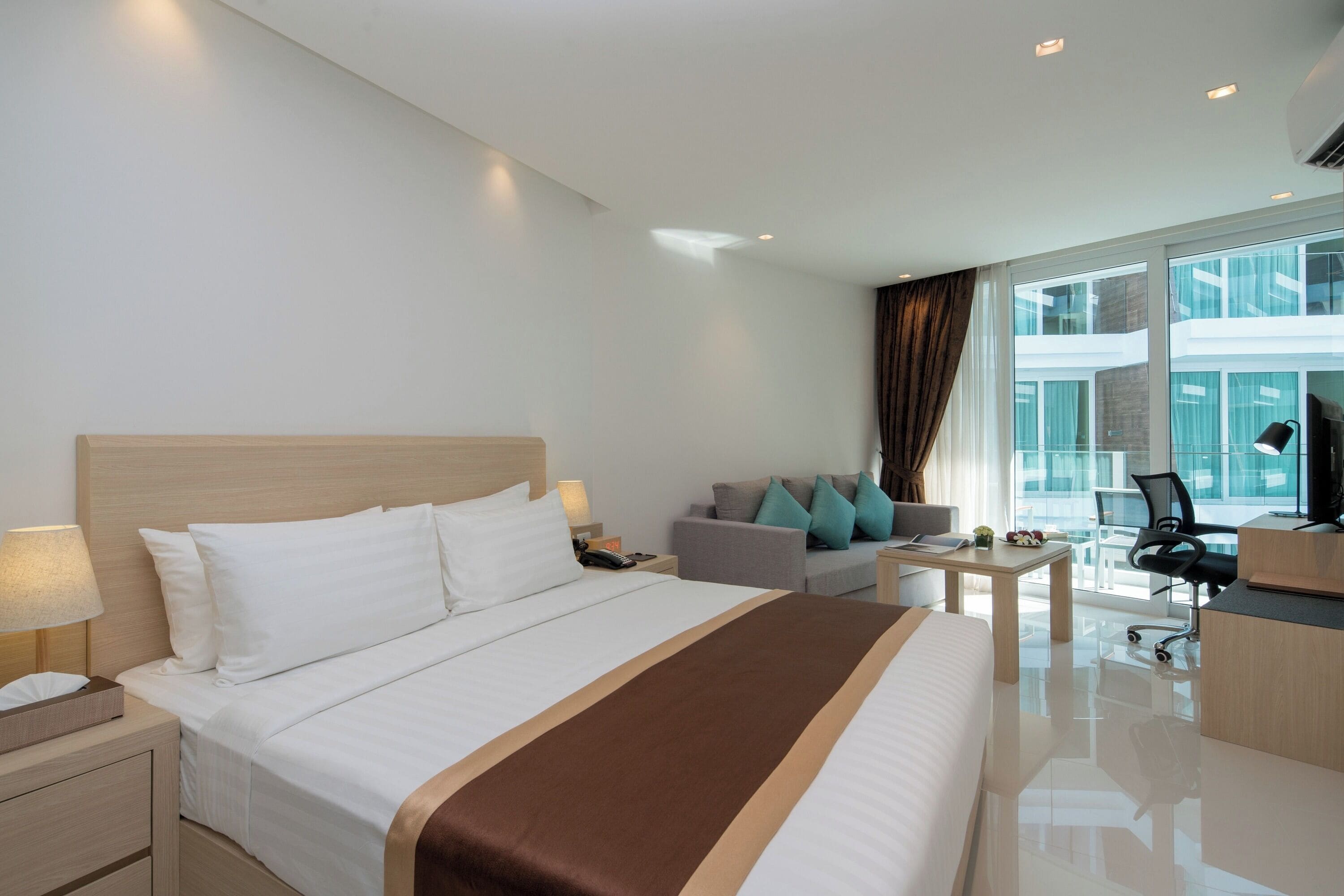 A modern hotel room with a large bed, a desk, a chair, and a sofa.