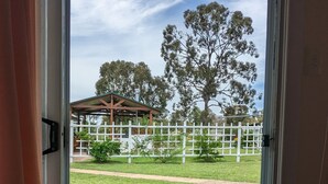 On aperçoit, à travers une porte vitrée, un espace extérieur verdoyant avec une clôture blanche, une structure en bois et des arbres.