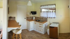 Une cuisine compacte dotée d’un plan de travail en bois, de meubles blancs, d’un petit réfrigérateur et d’une fenêtre avec des rideaux.