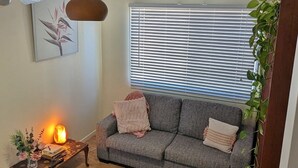 Un salon avec un canapé gris, un tapis à motifs, une petite table en bois sur laquelle est posée une bougie, et une plante.