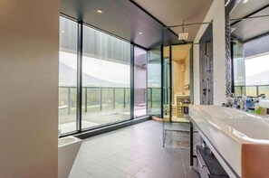 Un baño moderno con una bañera grande, un box de ducha de vidrio y vistas a la ciudad a través de amplios ventanales.
