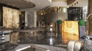 A modern lobby with a marble wall, a reception desk, and a seating area with a coffee table. - Hotel Emirates (Sofia)