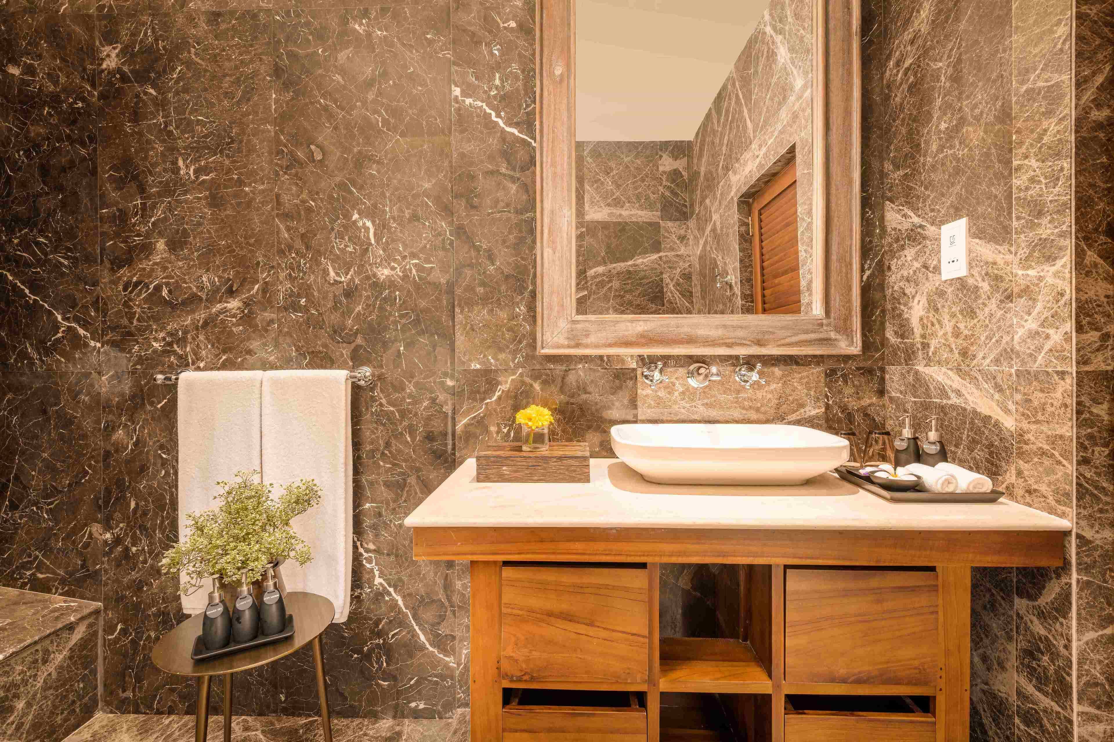 A bathroom with a marble wall, a wooden vanity, a sink, and a mirror.