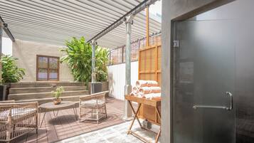 Ein überdachter Patio-Bereich mit Korbmöbeln, einem kleinen Tisch mit Pflanze und einer Bank.