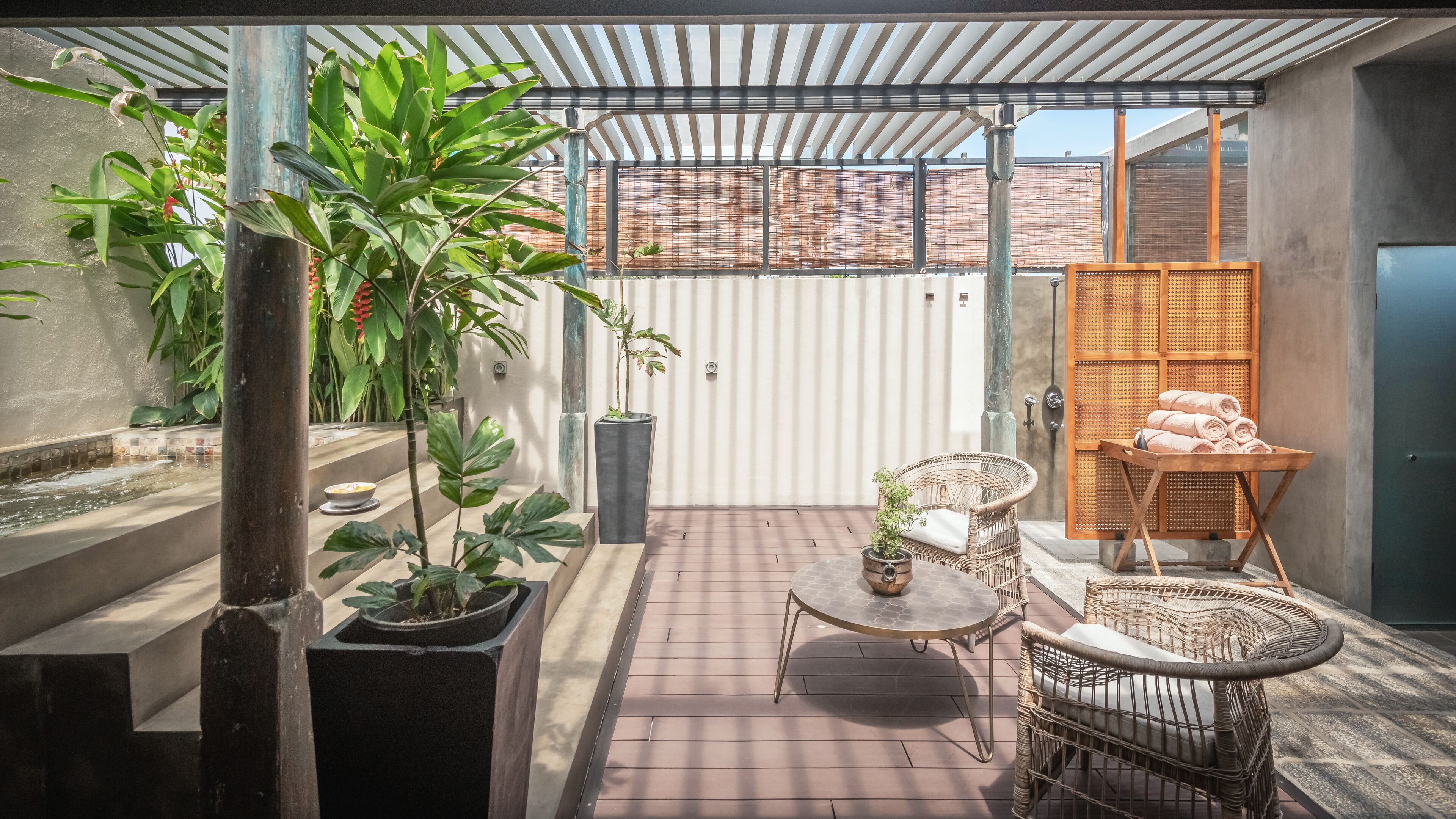 A covered patio with potted plants, a wicker chair, a small table, and a towel rack.