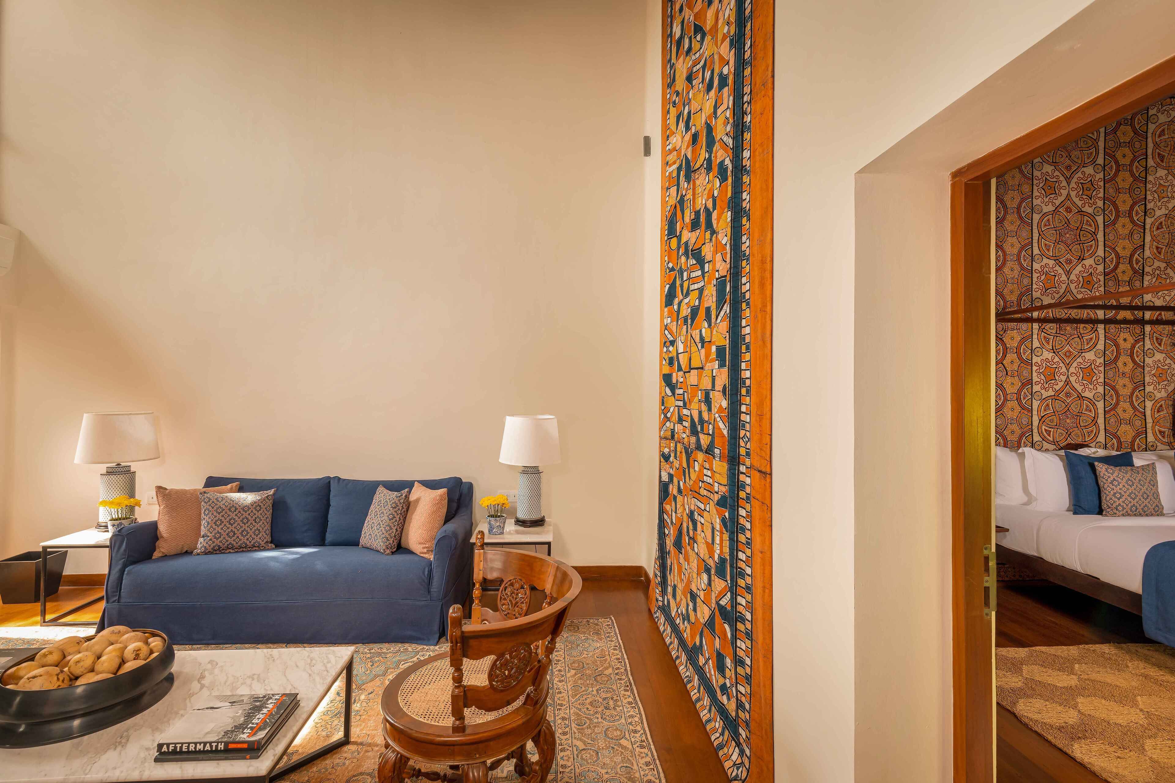 A living room with a blue sofa, a wooden chair, a coffee table with a bowl of snacks, and a lamp.