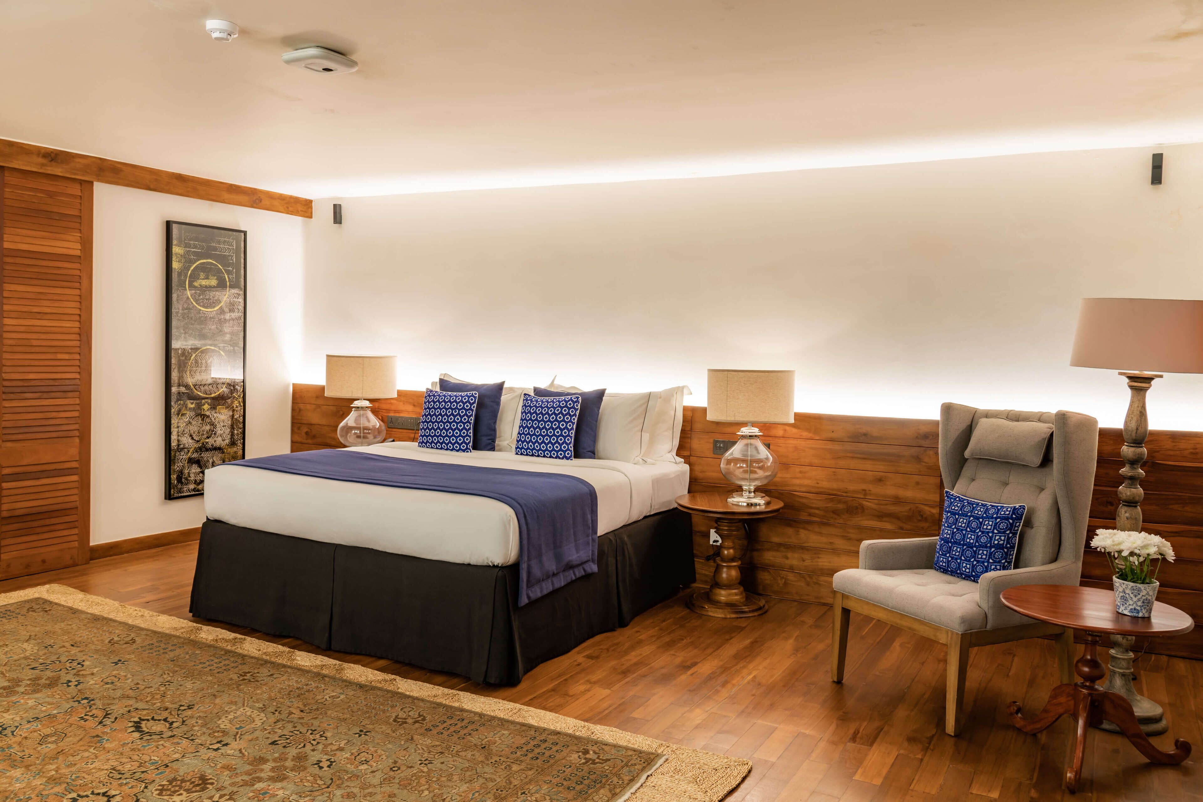 A hotel room with a large bed, two bedside tables with lamps, a chair, a small table with a vase, and a decorative wall piece.