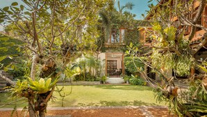 A lush garden with a variety of plants and trees, a well-maintained lawn, and a building with a traditional architectural style in the background.