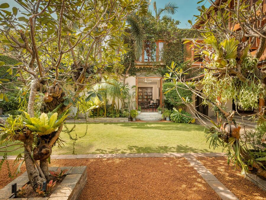 A lush garden with a variety of plants and trees, a well-maintained lawn, and a building with a traditional architectural style in the background.