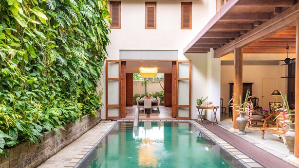 A pool with a wooden deck, surrounded by lush greenery and a traditional wooden structure.