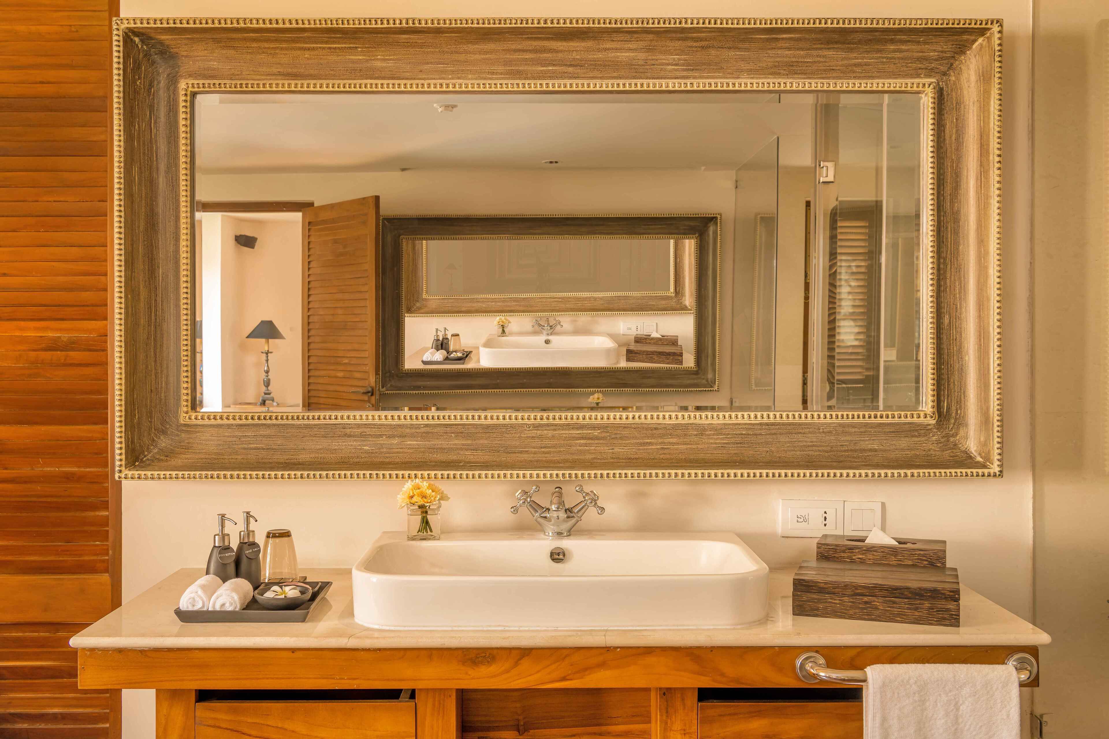 A bathroom with a large mirror, a sink, toiletries, and a towel rack.