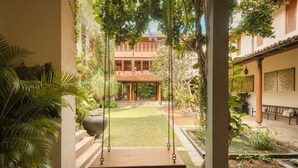 A courtyard with a swing set, a tiled patio, and a building with a tiled roof in the background.