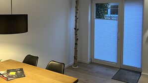 A dining area with a wooden table, chairs, a hanging light fixture, and a view of a balcony with a door and window blinds. - Vacation apartment Kurpark Brilon on the Rothaarsteig Start (Brilon)