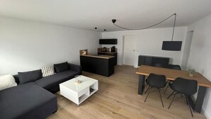 A modern living room with a black sofa, white coffee table, and a dining area with a wooden table and black chairs. - Vacation apartment Kurpark Brilon on the Rothaarsteig Start (Brilon)