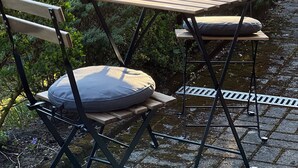 A patio with a wooden table and chairs, surrounded by lush greenery and a stone pathway. - Vacation apartment Kurpark Brilon on the Rothaarsteig Start (Brilon)