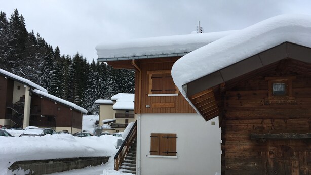 Eine Holzhütte mit schneebedecktem Dach, eine Treppe, die zu einem zweiten Stock führt, und ein Parkplatz mit Autos.