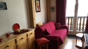 Ein gemütlicher Wohnbereich mit einem Holzschrank, einem roten Sofa und einem kleinen Hocker.
