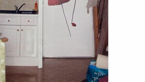 Ein Zimmer mit einer weißen Tür, einer Küchenzeile mit weißen Schränken und einer blauen Tasche auf dem Boden.