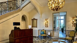 Un lobby espacioso con piso a cuadros, un mostrador de recepción de madera, una escalera y una gran lámpara de araña.