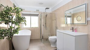 Bathroom features a bathtub, glass-enclosed shower, and white vanity with mirror.