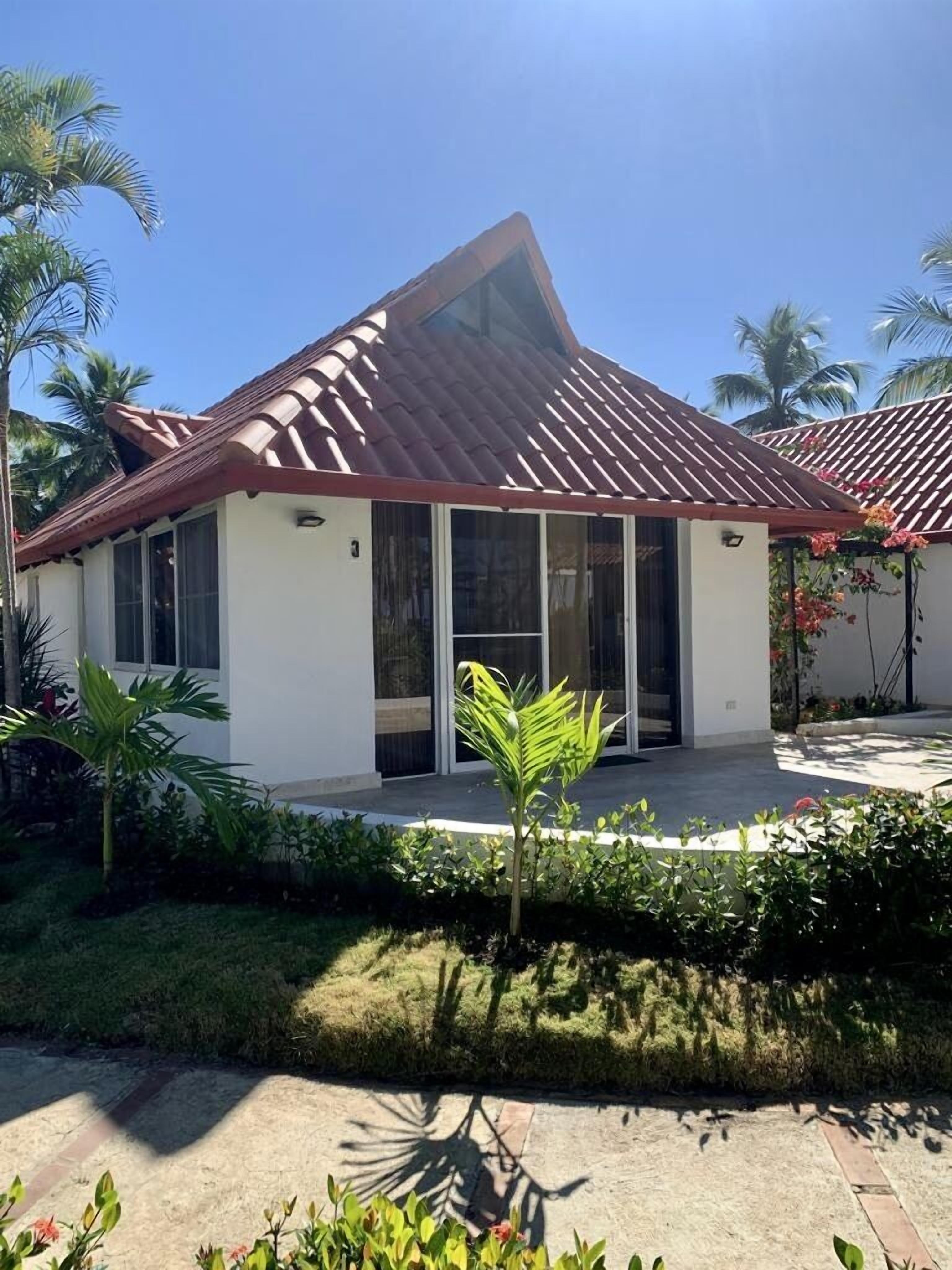 A single-story house with a red-tiled roof, large windows, and a small porch area.