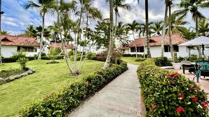 A pathway leading to a row of white buildings with red-tiled roofs, surrounded by palm trees and well-maintained greenery. - ON THE Cliff IN THE Caribbean SEA - Villa Ilaria (Boca Chica)
