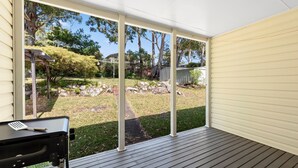 Un patio couvert donnant sur un jardin, avec un barbecue et une table.