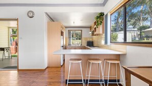 Une cuisine moderne avec des meubles en bois, un plan de travail blanc et trois tabourets de bar.