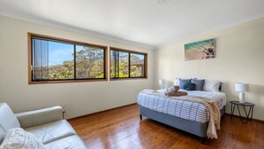 Une chambre à coucher avec un lit, deux fenêtres, un tableau, une chaise et une petite table.