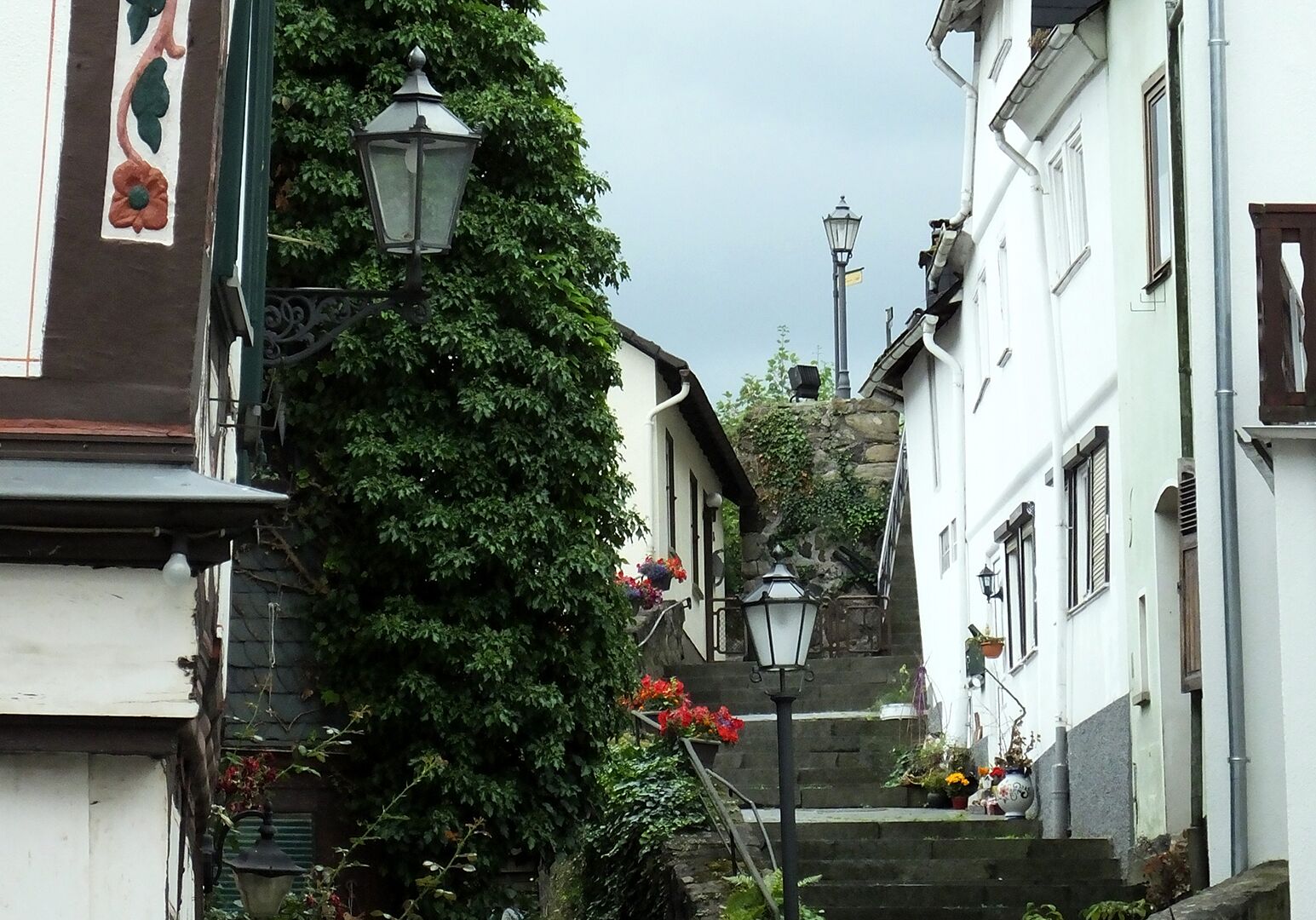 A narrow street with white buildings, a stone wall, and a street lamp.
